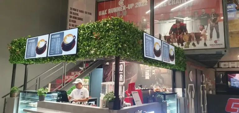 A man stands at a counter with LCD menu displays visible in the background of the restaurant.