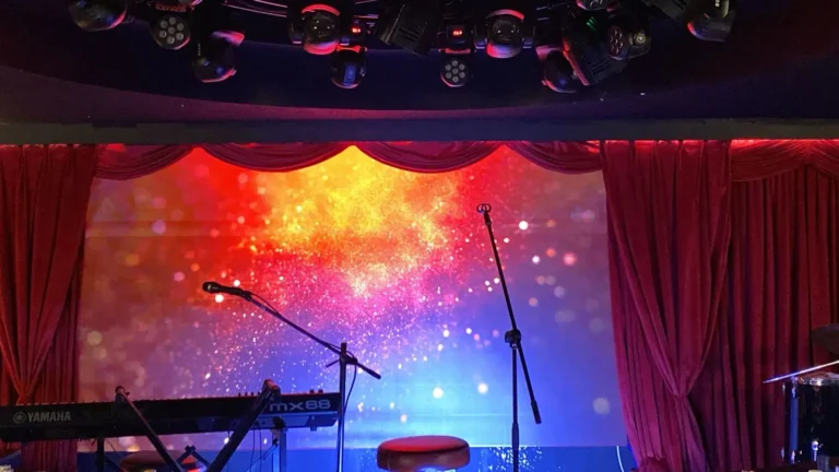 Indoor stage featuring red curtains and an LED screen for presentation.