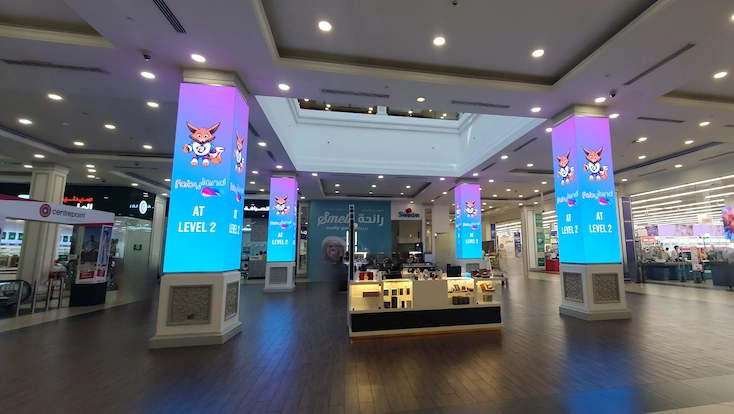 A mall scene featuring a large pillar LED display adorned with colorful lights.