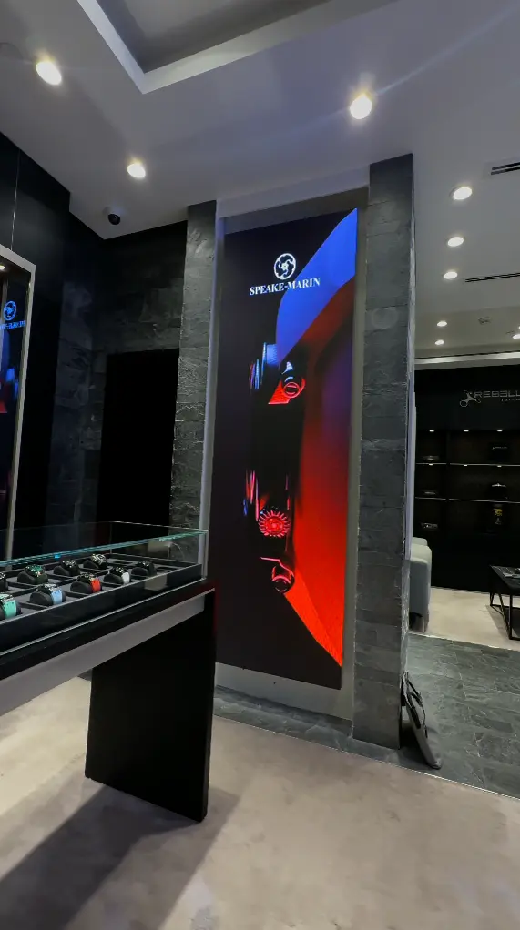 A watch display in a store, with an LED screen on the wall displaying current offers