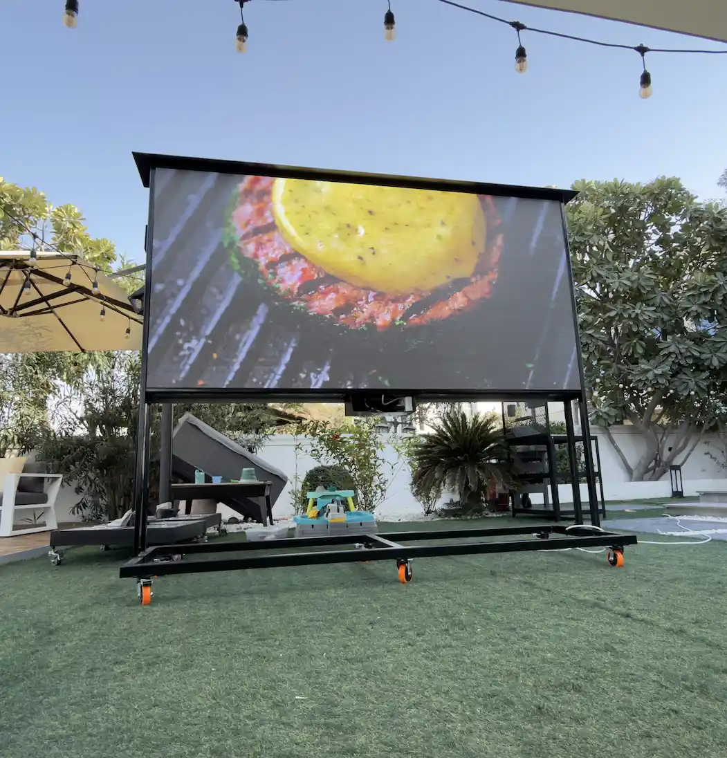 An outdoor digital signage screen set on a lawn beside a grill, ideal for outdoor events.