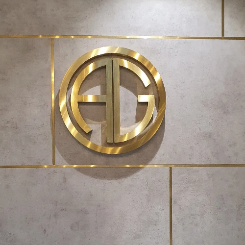 Polished gold AG monogram inside a circle, mounted on a grey tiled wall