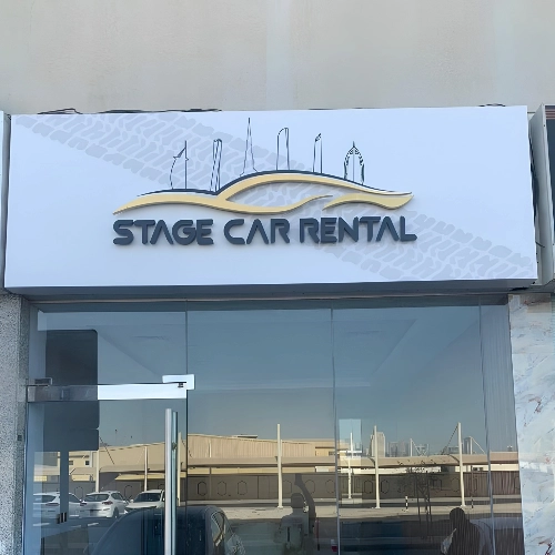Dark gold car logo for Stage Car Rental above a glass shop door
