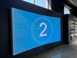 A wall-mounted LED video display showing a blue screen with the number 2 inside.
