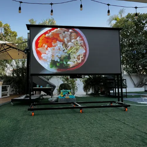 outdoor LED screen on a wheeled frame in a restaurant garden, showing a food video