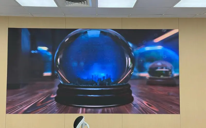 Wall-mounted indoor LED display showing a snow globe visual in an office