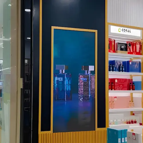 Wall-mounted indoor LED screen showing perfume ads in a retail store
